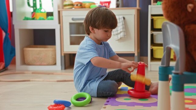 Boy stacking plastic rings with hand on foam mat in building playroom; concentration learning childhood.