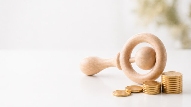 Wooden baby rattle with stacked gold coins symbolizing savings and plan for future financial security and child care happiness