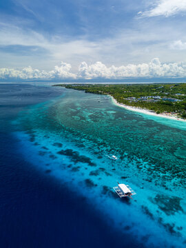Aerial view of Panglao Island with turquoise waters, coral reefs, and a traditional outrigger boat floating near the white sand beach in Bohol, Central Visayas, Philippines.