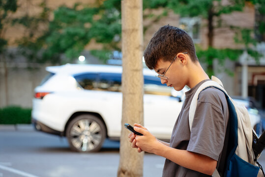 Side view of teen student with backpack standing near a city road and checking GPS route on smartphone after classes. Concept of navigation app, school commute, independent travel and safety.