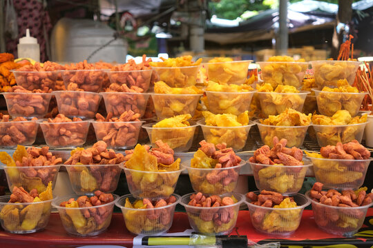 Assortment of fried snacks and sausages displayed in clear plastic cups at a market stall