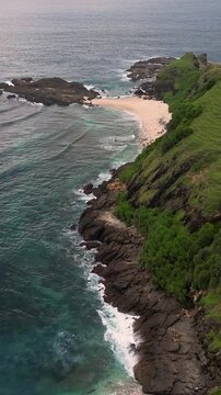 Aerial seascape turquoise bay with cliffs overlooking verdant grassy slopes, clear shallow reef patches,Bukit Merese, Lombok, Tanjung Ann, Indonesia,vertical video
