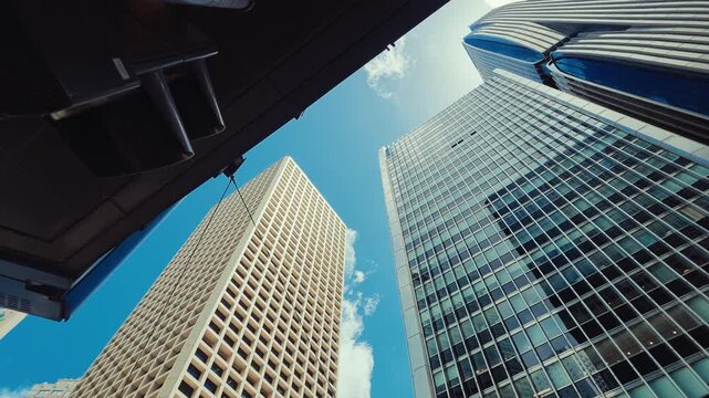 A panoramic view of modern Hong Kong's skyline, starting with a close-up on a beige building before slowly moving to reveal towering skyscrapers against a bright blue sky