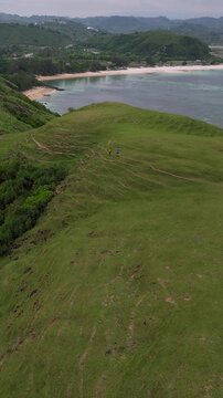 Aerial tropical beach cove with turquoise water and rocky headland waves breaking over coral reef, lush green vegetation cascading down cliffs, Bukit Merese, Lombok,Tanjung Ann, Indonesia