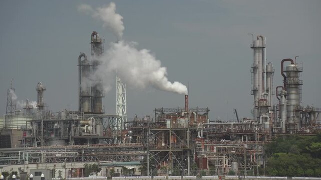 白い煙を上げて稼働する複雑な工場のプラント構造物、日本の工業地帯の日常