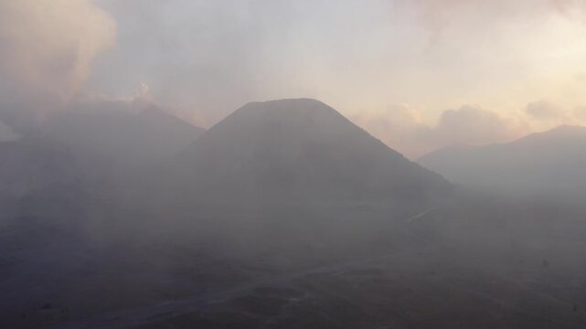 Aerial drone flies through low cloud toward Mount Bromo volcano at sunrise on a misty morning, East Java, Indonesia. Cinematic b-roll of a dramatic volcanic landscape.