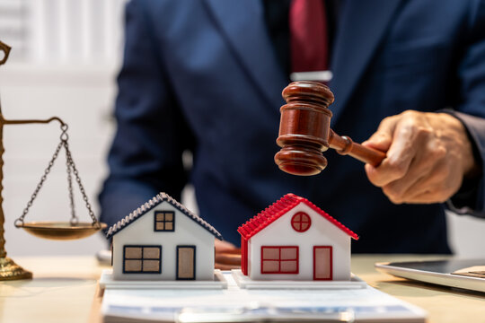 Lawyer holding gavel beside house models and scales of justice, showing property dispute or real estate law concept