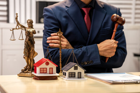 Businessman with gavel and justice statue beside model houses, showing real estate law, property dispute and legal advice concept.