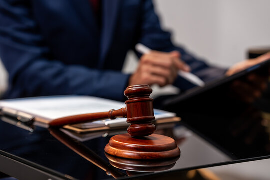 Wooden gavel on a desk with a lawyer working in the background, showing a legal office meeting, contract review, and justice concept.