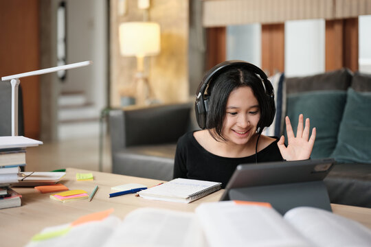 Asian teenage girl greeting in online class, remote learning at home using digital tablet, writing and reading textbooks, self-study for back to school, Homeschooling, university education lifestyle.