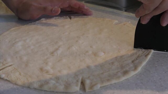 A close-up shot of raw, hand-stretched Italian pizza dough resting on a clean kitchen countertop, ready for toppings and baking. The scene captures the authentic process of preparing a traditional hom