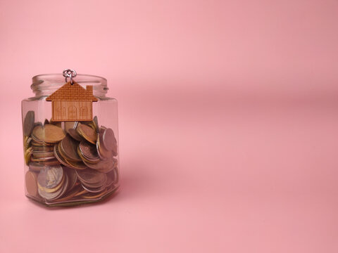 A glass jar packed tightly with metal coins features a wooden house-shaped charm attached to its rim