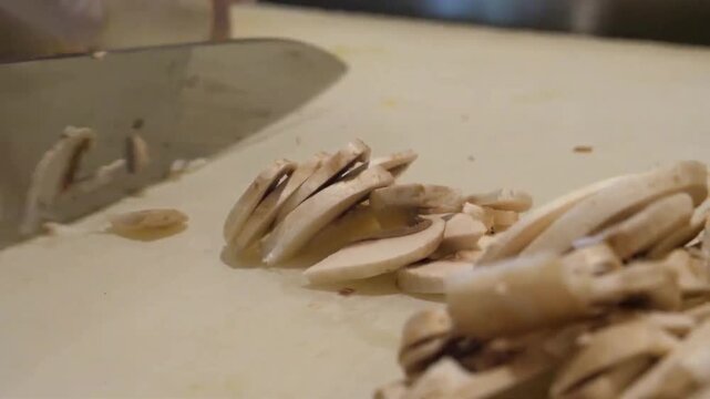 Close-up footage of a professional chef expertly slicing fresh white champignon mushrooms on a cutting board. High-quality b-roll perfect for culinary tutorials, Italian restaurant promotions, and hom