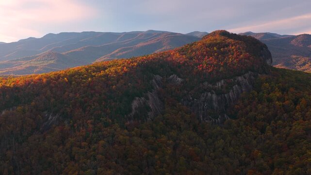Scenic sunset over Looking Glass Rock in Appalachian mountains in North Carolina. Massive granite boulder with dense woodland in fall season. Autumn foliage blankets hills with shades of colors.