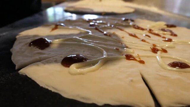 close-up, high-definition shot of a pizzaiolo's hands meticulously applying layers of red tomato sauce and white cream in a spiral pattern onto raw pizza dough. This footage captures the authentic cul