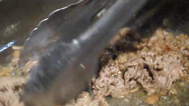 Detailed close-up footage of savory ground meat or Italian sausage being browned and crumbled in a frying pan using tongs. This essential step shows the preparation of fresh toppings for an authentic 