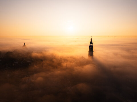 Aerial view of the Lange Jan abbey tower rising above a thick layer of morning fog at sunrise in Middelburg, Zeeland, Netherlands.