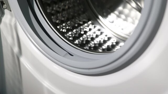 Close-up shot of a shiny washing machine drum. Detailed view moving inside the empty, stainless steel drum of a modern washing machine, highlighting its honeycomb texture and the reflective metallic