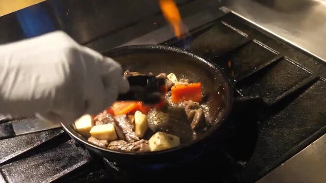 close-up shot of seasoned beef cubes and colorful vegetables, including red bell peppers and onions, being tossed and saut&eacute;ed in a hot pan over a professional stovetop with visible steam. High-end cul