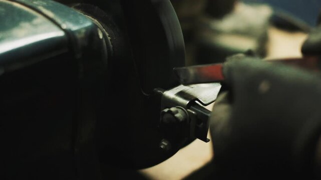 Closeup bench grinder sharpening blade produces sparks while operator hones edge, dark workshop atmosphere, textured metal