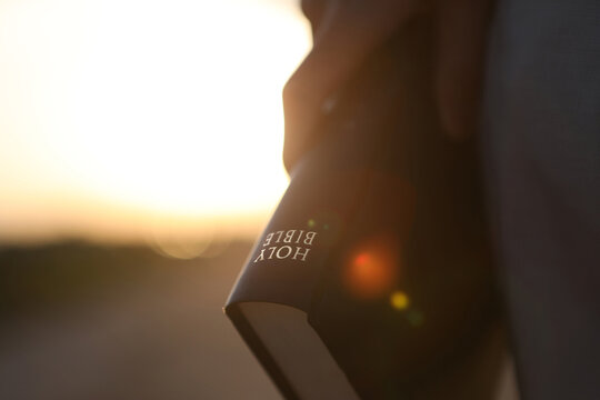 A Christian holding the holy Bible, the word of truth; background of faith, belief, worship, and prayer.

