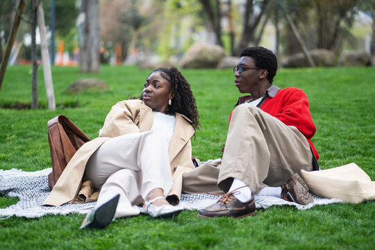 Relaxed carefree african american couple man and woman friends resting outdoors on grass in park, chill black male and female partners on date relaxing on plaid in city garden enjoying warm weather.