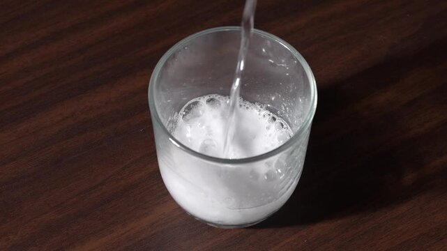 Angled top view of pouring carbonated sparkling water into glass cup