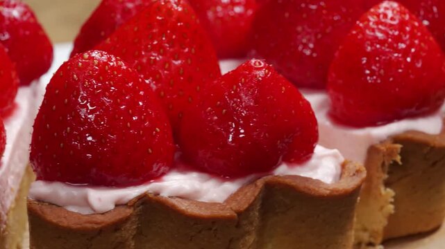 High-quality close-up footage of a decadent strawberry tart. The dessert features large, whole, glossy strawberries arranged over a smooth layer of light pink cream, nestled in a fluted golden shortcr