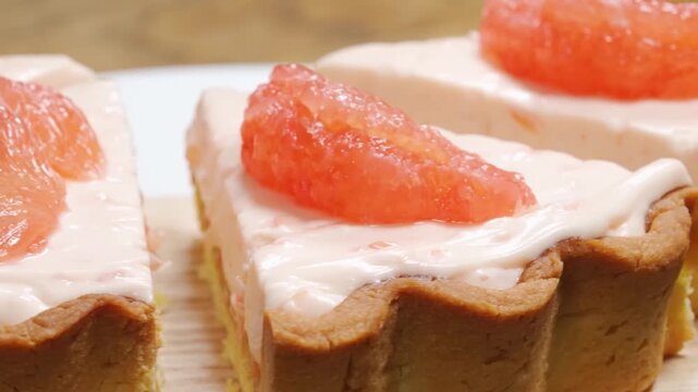 Close-up footage of delicious gourmet dessert slices featuring a buttery, fluted shortbread crust and a smooth, pale-pink citrus cream filling. Each slice is garnished with a juicy, vibrant pink grape