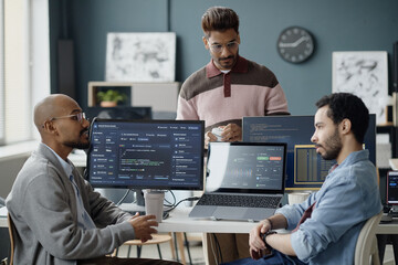 Multiethnic young adult men discussing software development workflow in information technology office, reviewing code and analytics dashboards. Ideal for teamwork, coding, startup marketing © Seventyfour