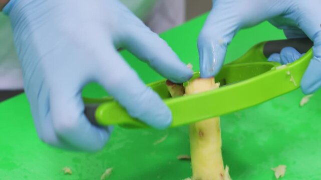 A close-up shot of a chef's hands in blue protective gloves using a green multi-blade fruit slicer to perfectly section a peeled fruit, such as an apple or mango, on a green prep surface. This high-qu