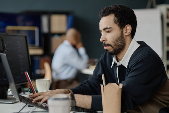 Medium shot of young adult man typing on laptop in information technology office, focusing on software work and productivity. Ideal for IT services, coding, digital workflow marketing