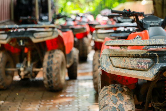 All terrain vehicle with muddy tires parked in row on wet paved surface under natural light, showing outdoor adventure and rugged transportation