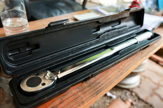 Chrome torque wrench in black case on wooden table, shiny metal tool for precise tightening, workshop equipment with clear glass in background, bright natural light