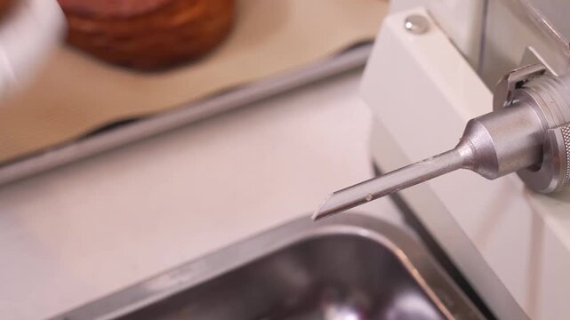 Close-up of a worker in a professional confectionery facility using an automated injection machine to fill a freshly baked, crispy puff pastry turnover with sweet cream or jam. High-quality footage sh