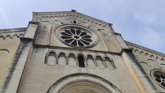 Camera tilts up the facade of a historic stone church with rose window details, Montpellier France