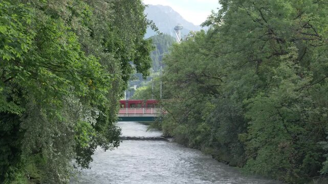 Trams pass bridge over fast flowing Sill River, Alps and ski jump Bergisel beyond.