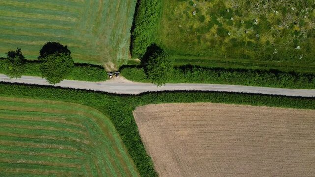 Top down drone shot of a single lane country road cutting between patterned crop fields and hedgerows in East Devon countryside.
