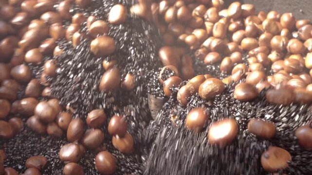 Extreme macro close-up reveals the abstract interplay of glossy roasted chestnuts and shimmering metallic roasting strands, creating an organic, textural pattern of brown and silver tones in motion