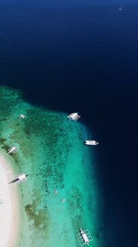 Vertical drone descends in a top-down orbit while tracking a boat approaching Public Pamilacan Beach in Bohol