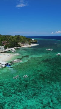 Vertical drone orbits two kayakers, then pulls back and ascends over Public Pamilacan Beach, showing reef, boats, and shore