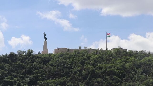 Shot of the iconic Liberty Statue and the Citadella fortress on top of Gellert Hill with the Hungarian flag waving in Budapest, Hungary.