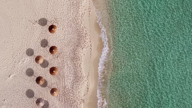 Straw umbrellas at empty beach near the shore, Simos beach, Elafonisos island, Overhead drone shot