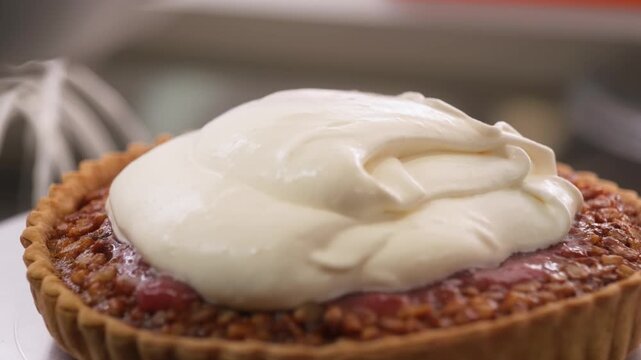 cinematic close-up shot capturing a dollop of thick, luscious whipped cream being spread over a red fruit jam filling in a golden-brown shortbread crust. This gourmet dessert tart, similar to a French