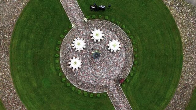 Drone video captures a circular garden plaza with decorative tables and central fountain, bordered by lush green lawns and stone paths, in soft overcast daylight, revealing careful symmetry.