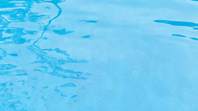 Clear blue swimming pool water background with gentle ripples and reflections on a sunny day.