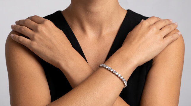 Lady in classic black fashion wear, wearing diamond tennis gemstone bracelet, embracing shoulders with hands, neutral plain studio setting, luxury accessory photography