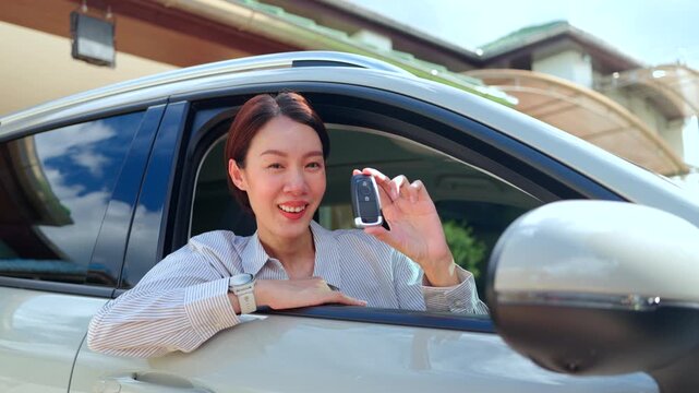 Smiling Asian woman sitting in an electric car and showing a smart key. Concept of buying a new EV car ownership auto insurance and happy driver lifestyle.