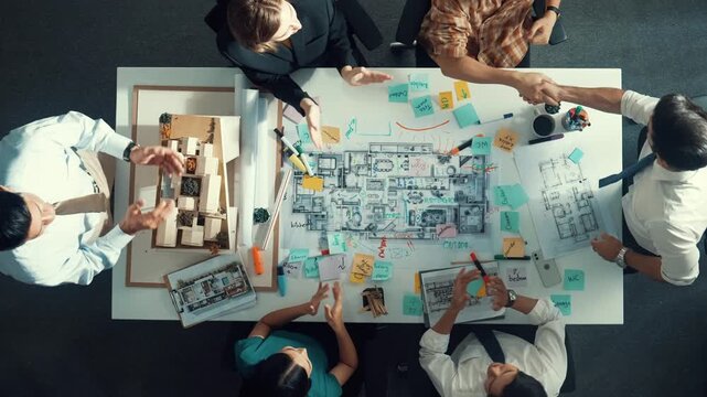 Top aerial view of manager shaking hand and making contract at meeting table with blueprint and house model. Group of diverse people working together and celebrate successful project. Alimentation.