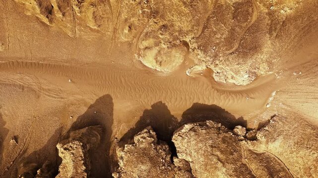 Aerial view of sandy canyon floor with textured wind-blown sand ripples and rock formations.